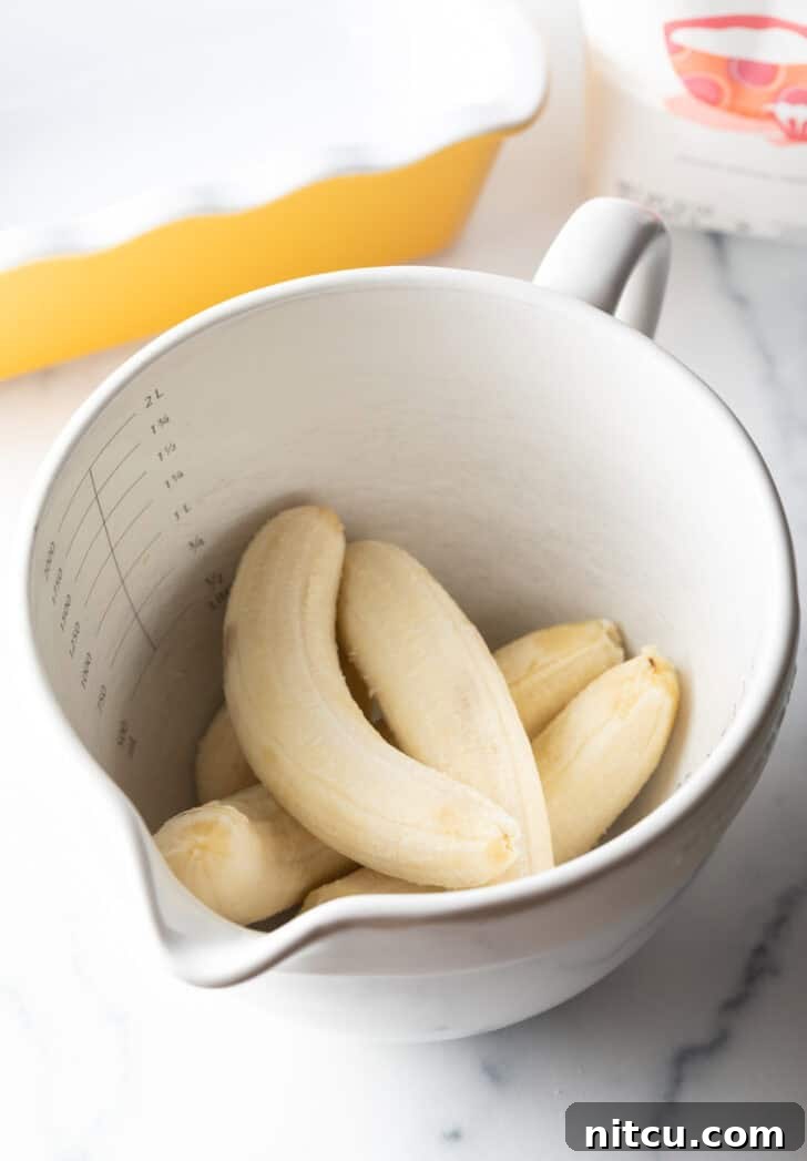 Effortless Banana Bread 6 Five peeled ripe bananas in a large white mixing bowl, ready to be mashed.