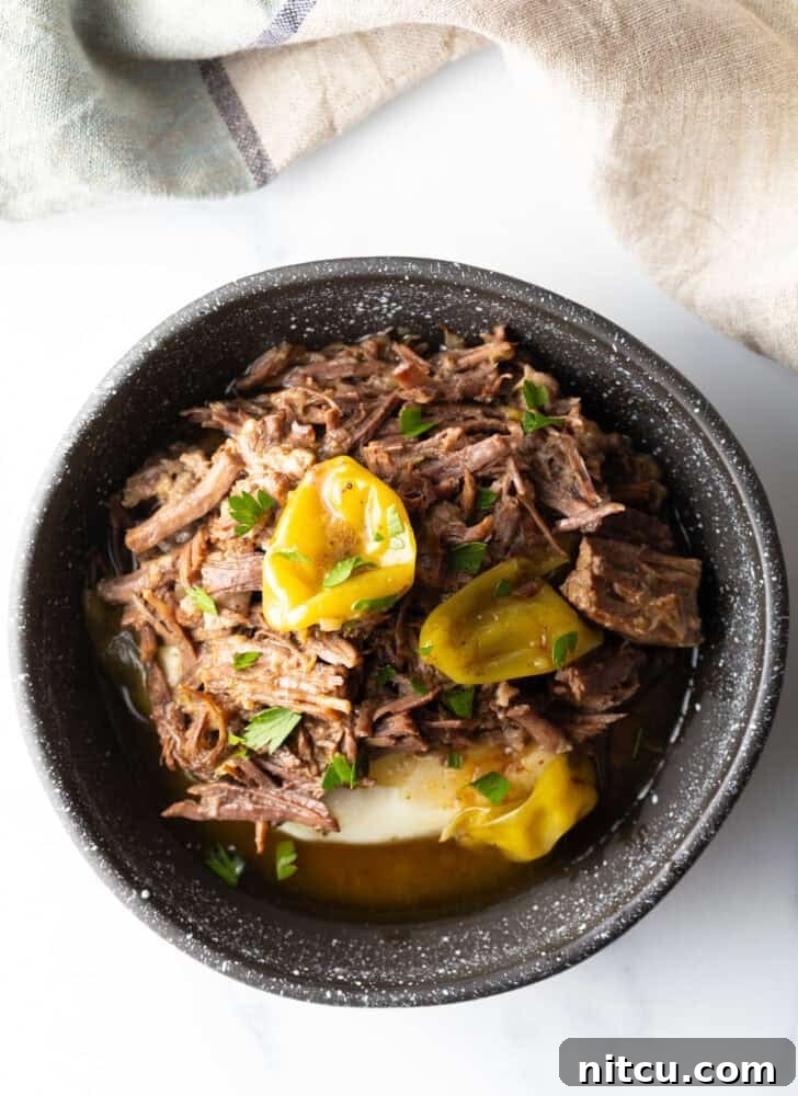 Melt-in-Your-Mouth Mississippi Pot Roast 4 Top down view of a black bowl with a layer of mashed potatoes topped with shredded pot roast and pepperoncinis.