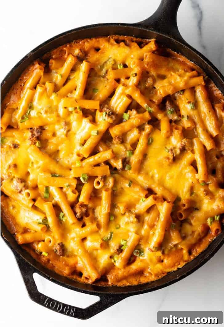 Homestyle Beef Bake 2 Top deep black cast iron skillet with long noodles, ground beef, and cheese. A perfectly cooked and bubbling cheeseburger casserole, ready to serve.