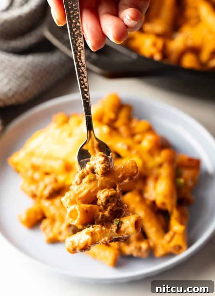 Homestyle Beef Bake 15 Hand holding a forkful of hamburger casserole to camera. The cheesy noodles and beef are prominent.