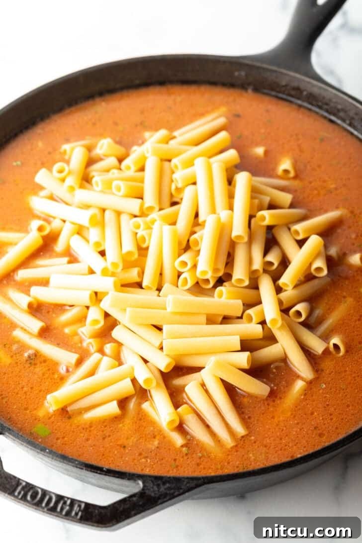 Homestyle Beef Bake 8 Adding long pasta noodles to a skillet with ground beef and tomato sauce. The pasta is raw and will cook directly in the sauce.