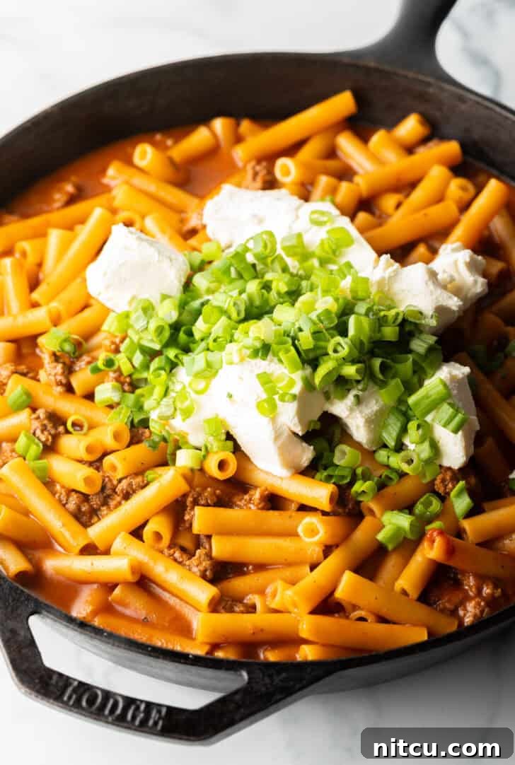 Homestyle Beef Bake 9 Adding cream cheese and chopped green onions to a cast iron skillet with ground beef and noodles. The cream cheese is cubed for quick melting.
