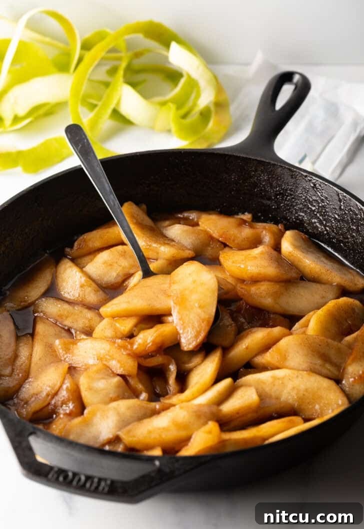 Caramelized Apple Bliss 10 A spoon gently stirring the apple slices in the skillet as they cook, ensuring even coating.