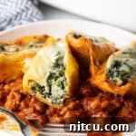 4 stuffed shells with spinach and meat sauce on a white plate.