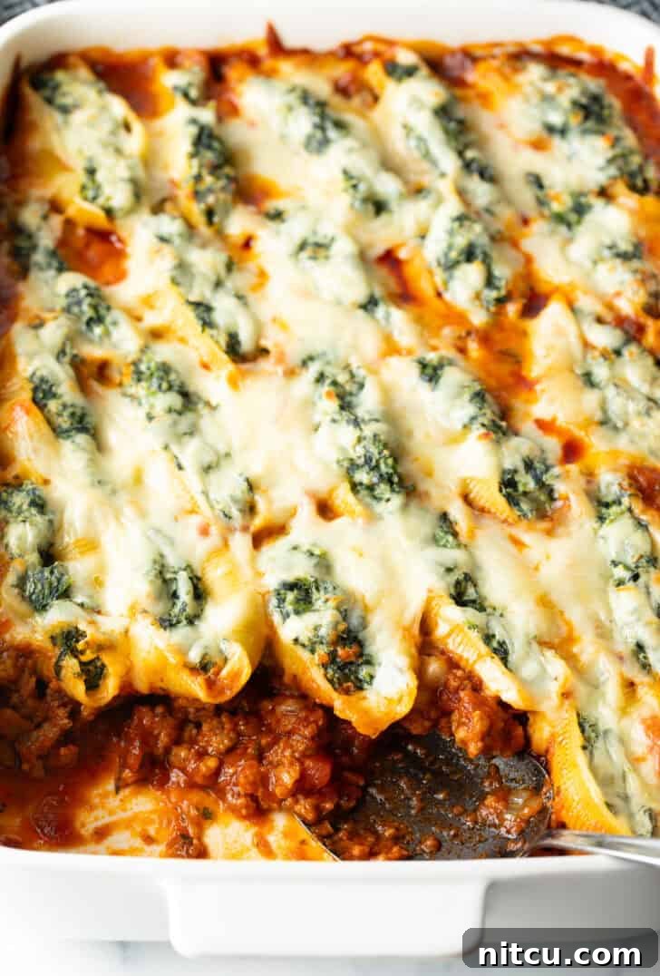 Top down view large rectangle baking dish with spinach and meat stuffed shells, with a serving taken out.