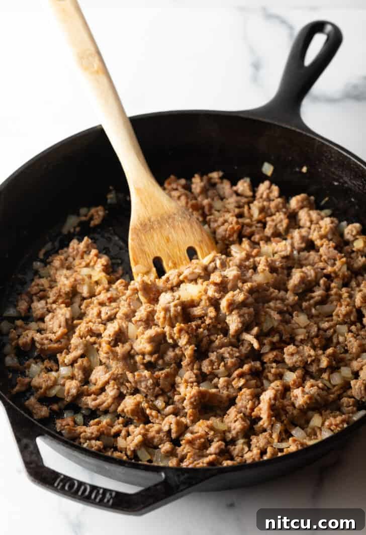 Browning ground beef in a large cast iron skillet with a wooden spatula.