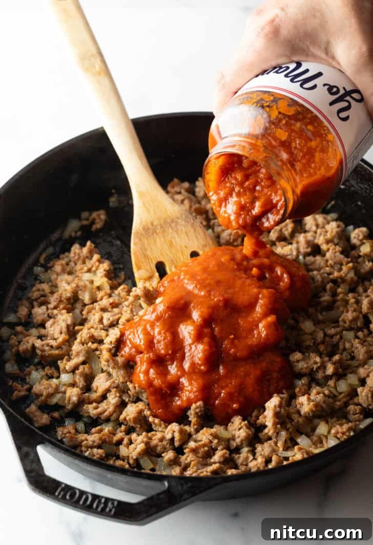 Adding jarred sauce to ground beef in a skillet.