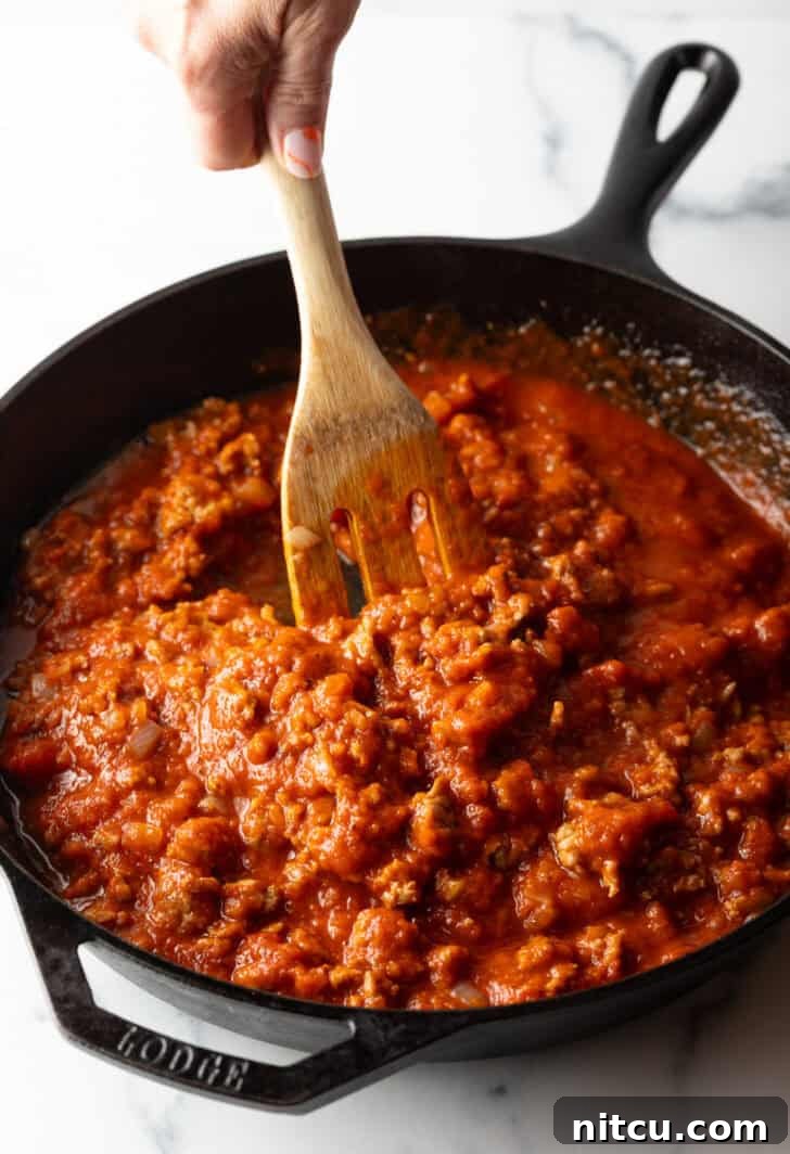 Using a wooden spatula to stir meat sauce in a cast iron skillet.