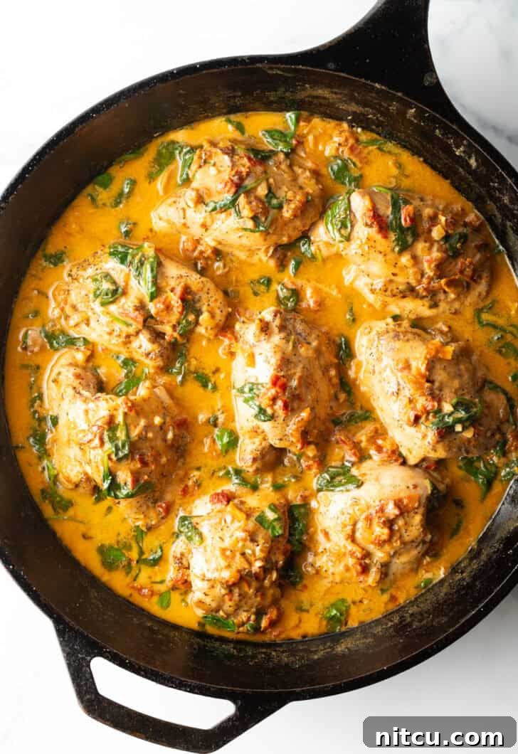 Top down view cast iron skillet packed with chicken thighs in a creamy Tuscan cream sauce.