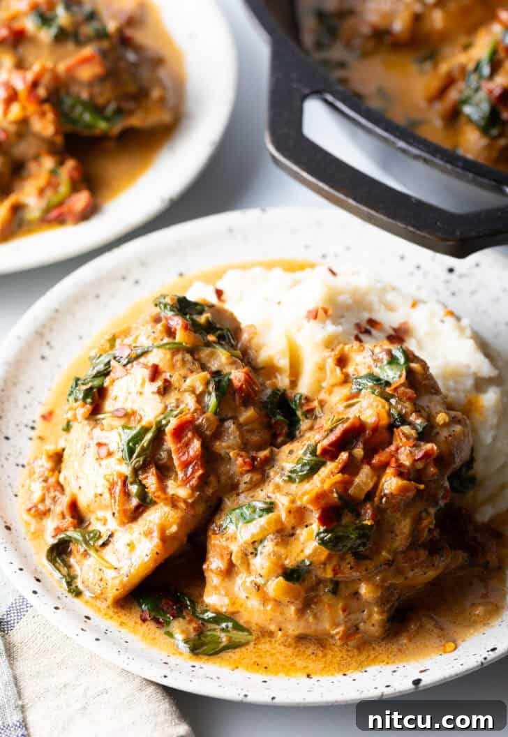 Two pieces of Tuscan chicken on a plate with mashed potatoes and creamy gravy.