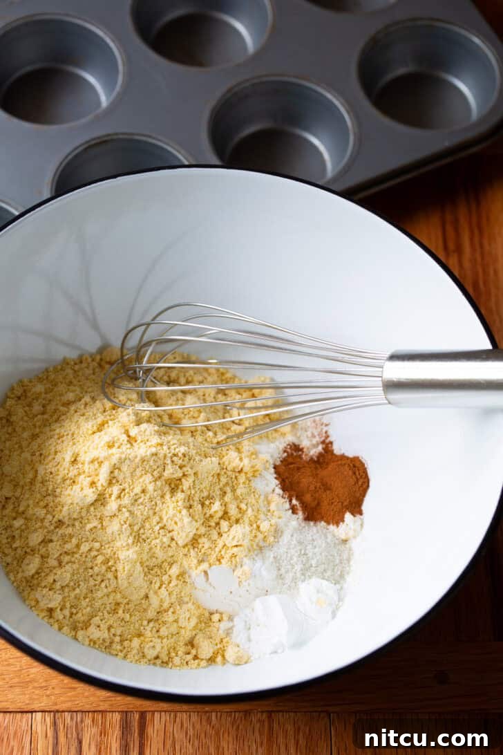 Golden Cornbread Gems 6 Dry ingredients for honey cornbread muffins, including cornmeal, flour, and cinnamon, perfectly blended in a white mixing bowl with a whisk.
