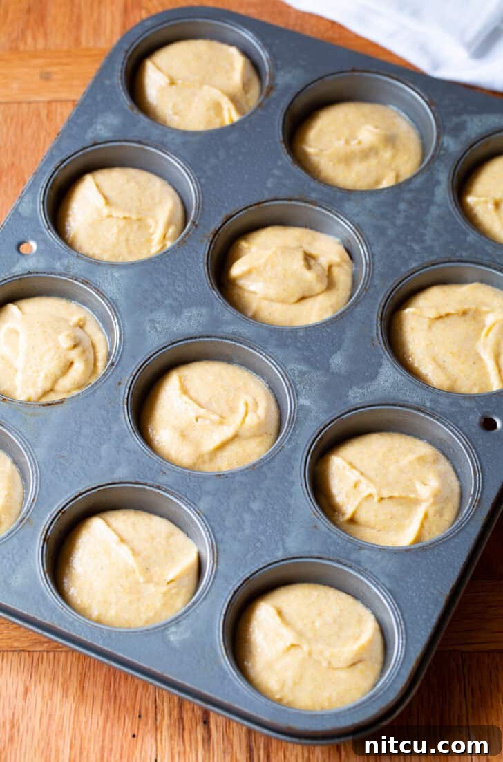 Golden Cornbread Gems 7 Smooth, golden corn muffin batter evenly distributed into a 12-cup baking tin, ready to be baked into delicious muffins.