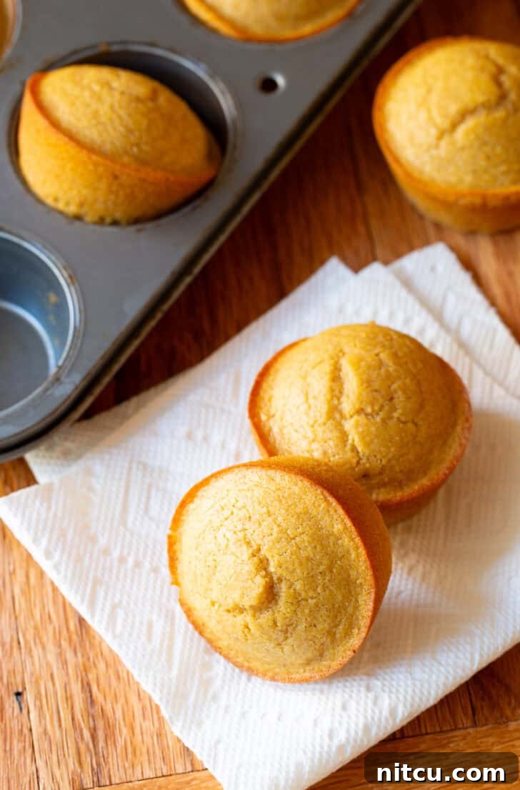 Golden Cornbread Gems 8 Two warm honey cornbread muffins on a white napkin, nestled beside a muffin baking tin overflowing with more freshly baked, golden muffins.