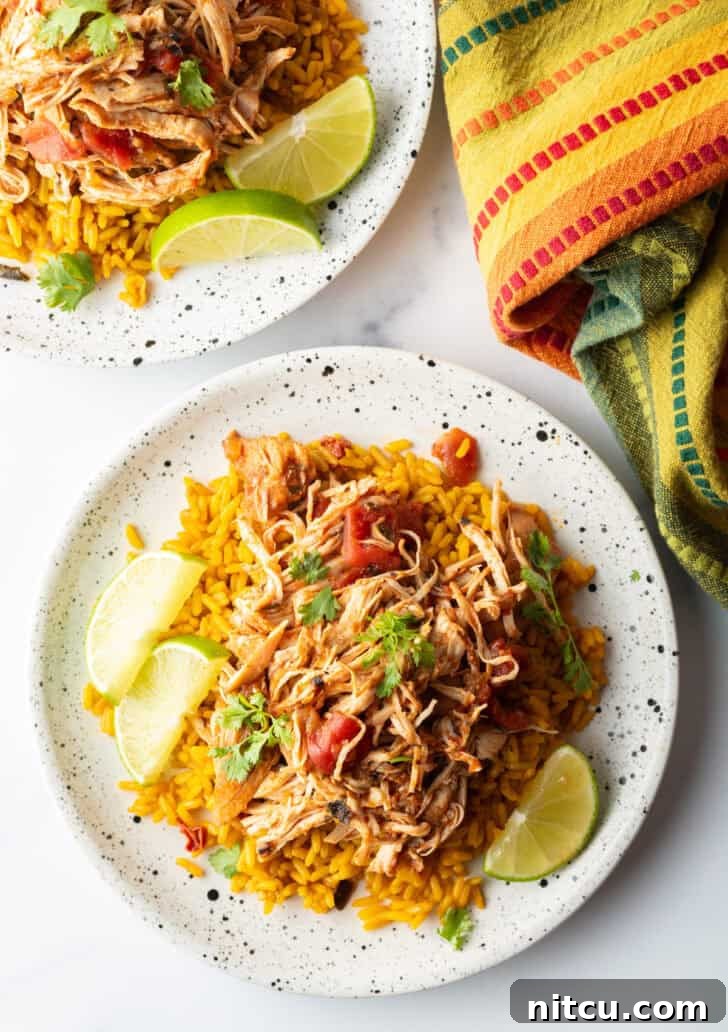 Fiesta Slow Cooker Chicken 12 Top down view mound of zesty shredded Mexican chicken on a plate with spanish rice and lime wedges.