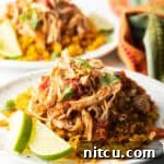 Mound of zesty shredded Mexican chicken on a plate with spanish rice and lime wedges.
