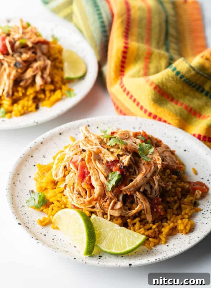 Fiesta Slow Cooker Chicken 5 Mound of zesty shredded Mexican chicken on a plate with spanish rice and lime wedges.