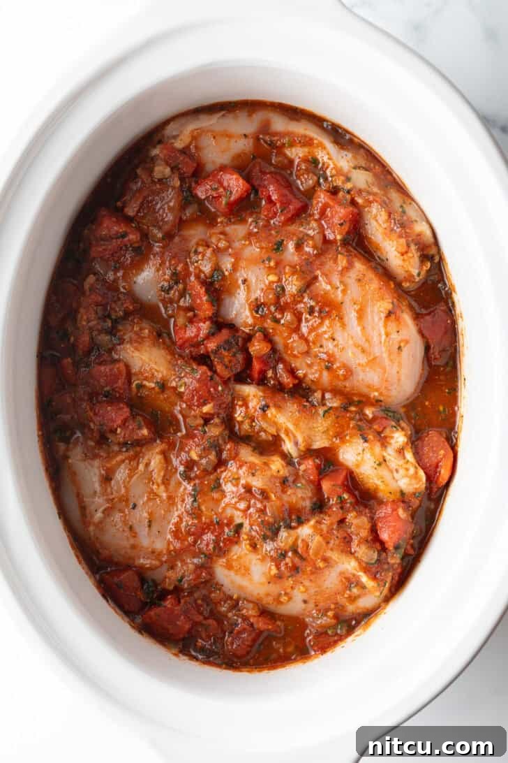 Fiesta Slow Cooker Chicken 8 Several whole chicken breasts covered in red sauce in a white crockpot.