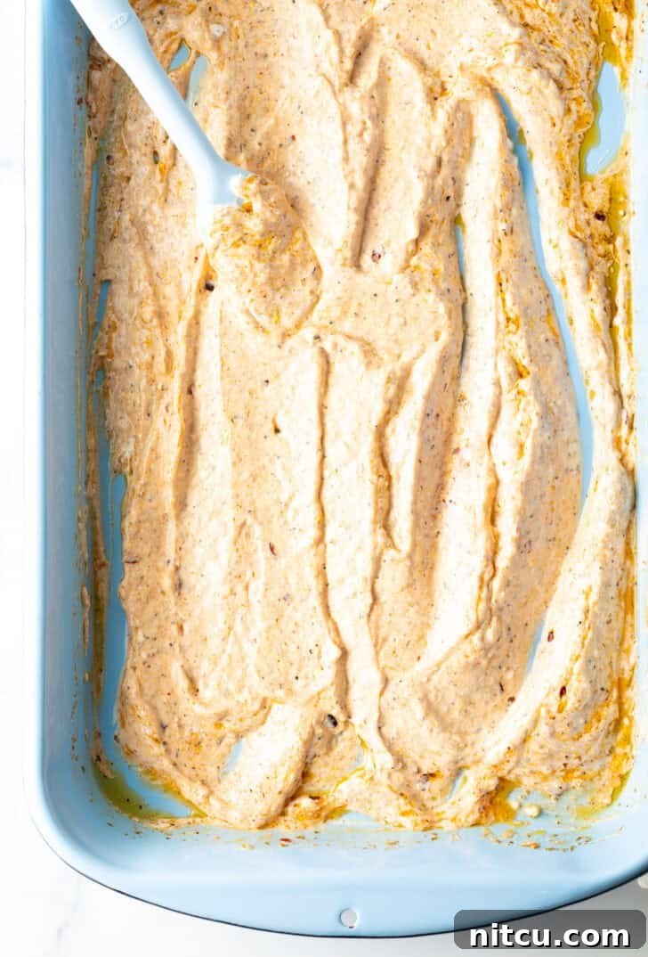 Top down view of a blue spatula spreading yogurt marinade in the bottom of a blue rectangle baking dish.