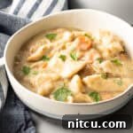 Effortless Slow Cooker Chicken and Dumplings 14 White bowl with crock pot chicken and dumplings sprinkled with fresh chopped parsley.