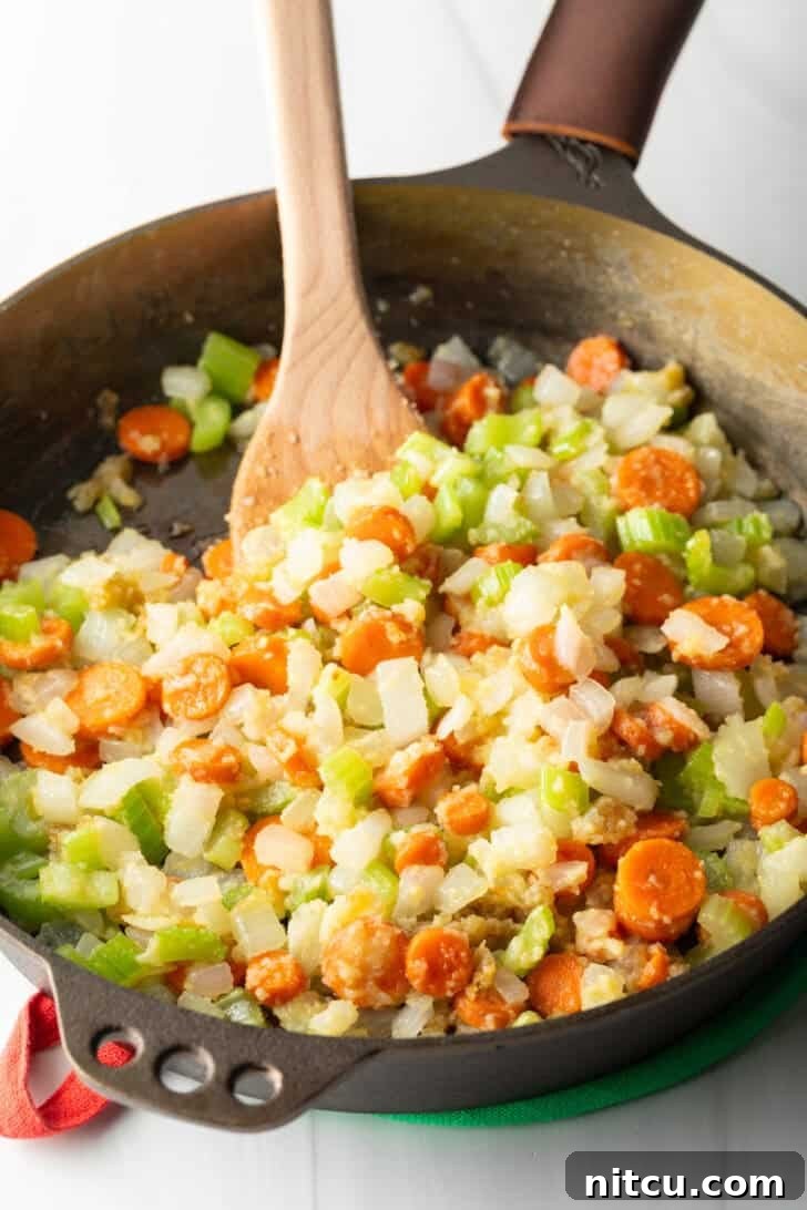 Effortless Slow Cooker Chicken and Dumplings 5 Chopped carrots, celery, and onion being sautéed in a cast iron skillet, releasing their sweet aromas.
