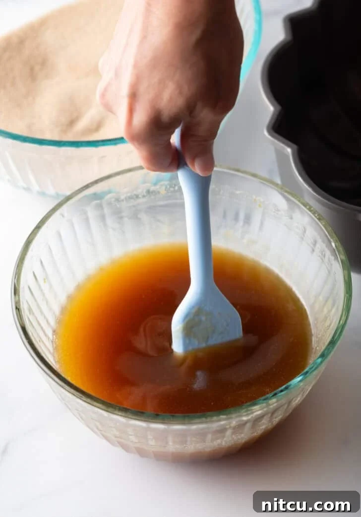 Irresistible Monkey Bread Delight 11 Stirring melted butter, brown sugar, and bourbon with a pastry brush in a glass bowl.
