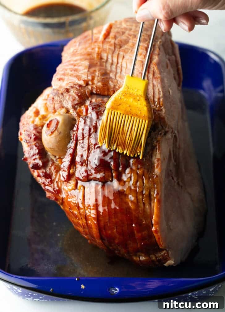 Perfect Spiral Ham Recipe 8 A cooked spiral ham being basted with a rich, golden sauce using a yellow silicone brush, highlighting the glazing process.