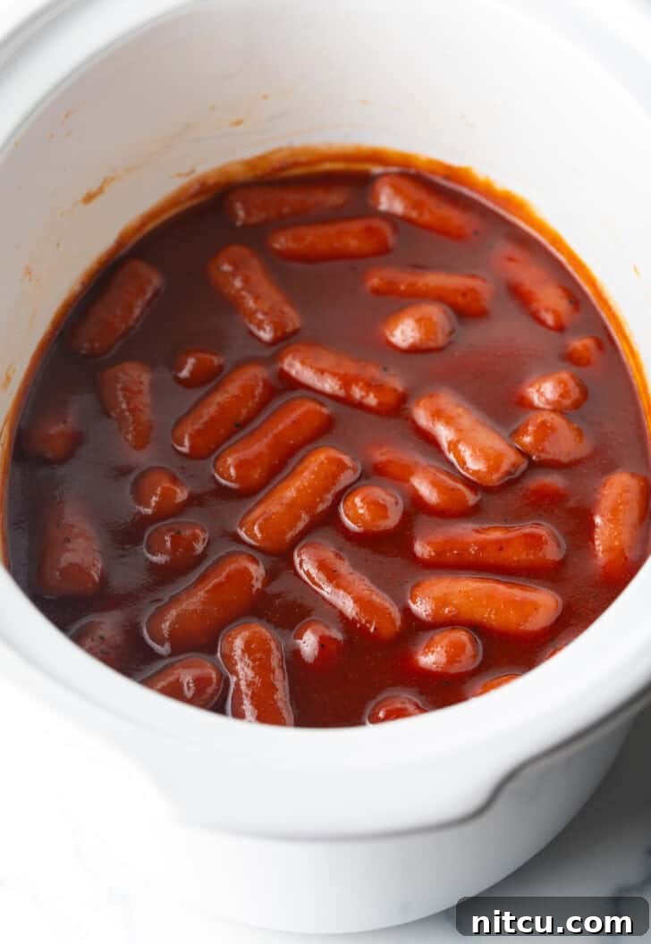 Glazed Cocktail Smokies 9 Little smokies in barbecue sauce in a white crock pot.