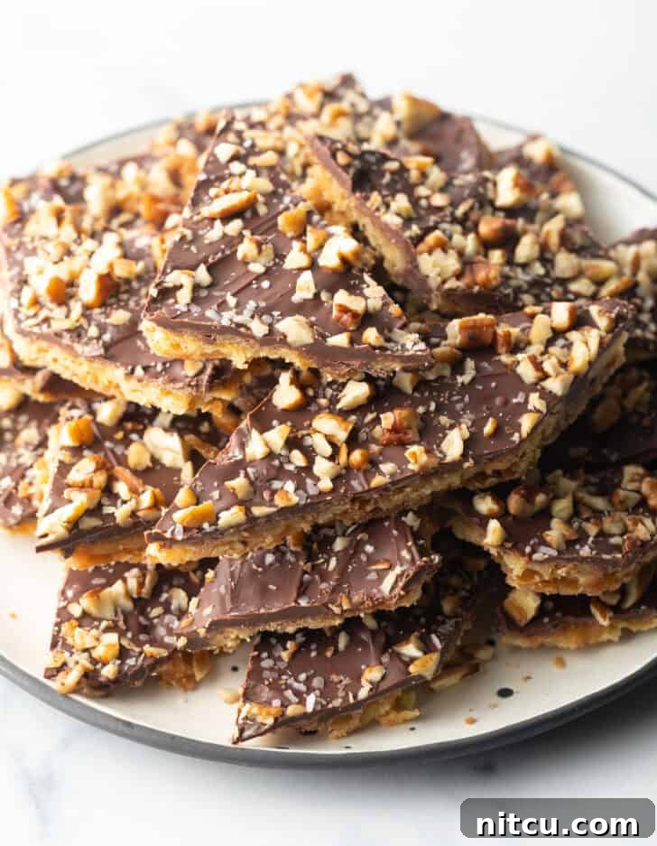 Pieces of salted toffee and chocolate candy aka Christmas crack piled up and stacked on a white plate.