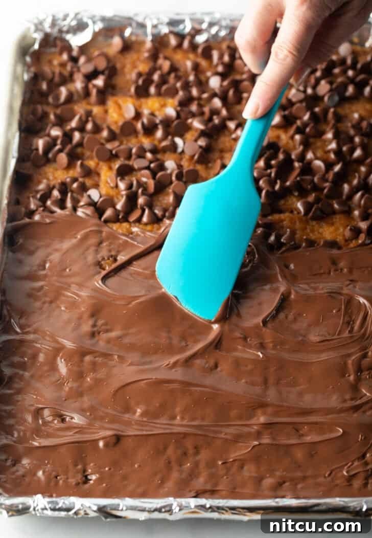 Using a blue spatula to spread melted chocolate over saltine crackers in a baking sheet.