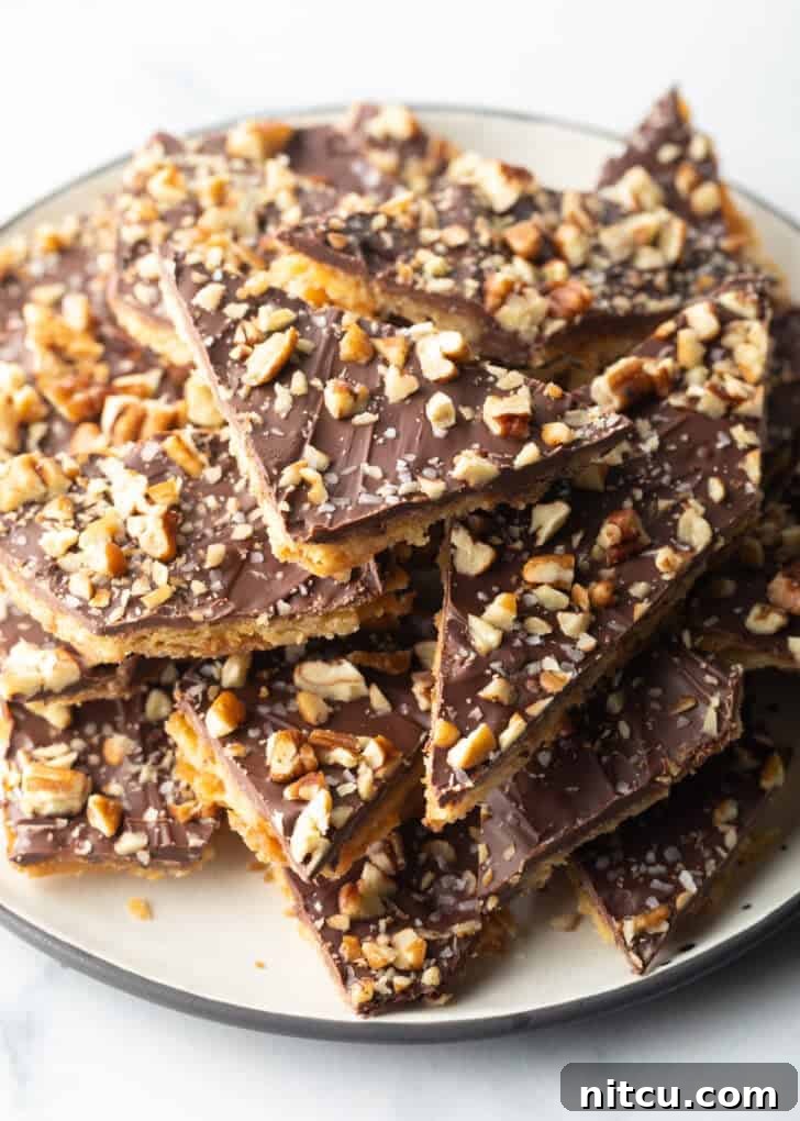Overhead view pieces of salted toffee and chocolate candy aka Christmas crack piled up and stacked on a white plate.