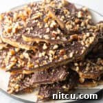 Pieces of salted toffee and chocolate candy aka Christmas crack piled up and stacked on a white plate.