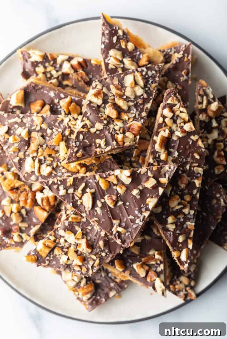 Overhead view pieces of salted toffee and chocolate candy piled up and stacked on a white plate.