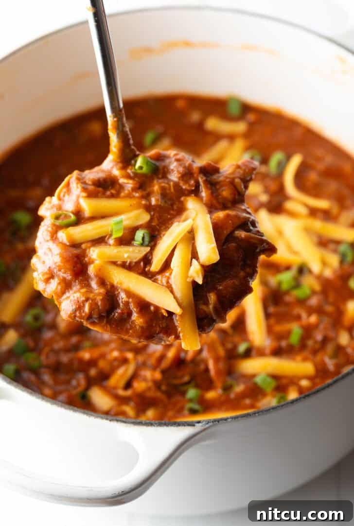 Easy 5 Ingredient Chicken Chili 2 A ladleful of rich chicken chili, generously topped with shredded cheddar cheese, held up to the camera with steam gently rising, highlighting its warmth and appetizing texture.