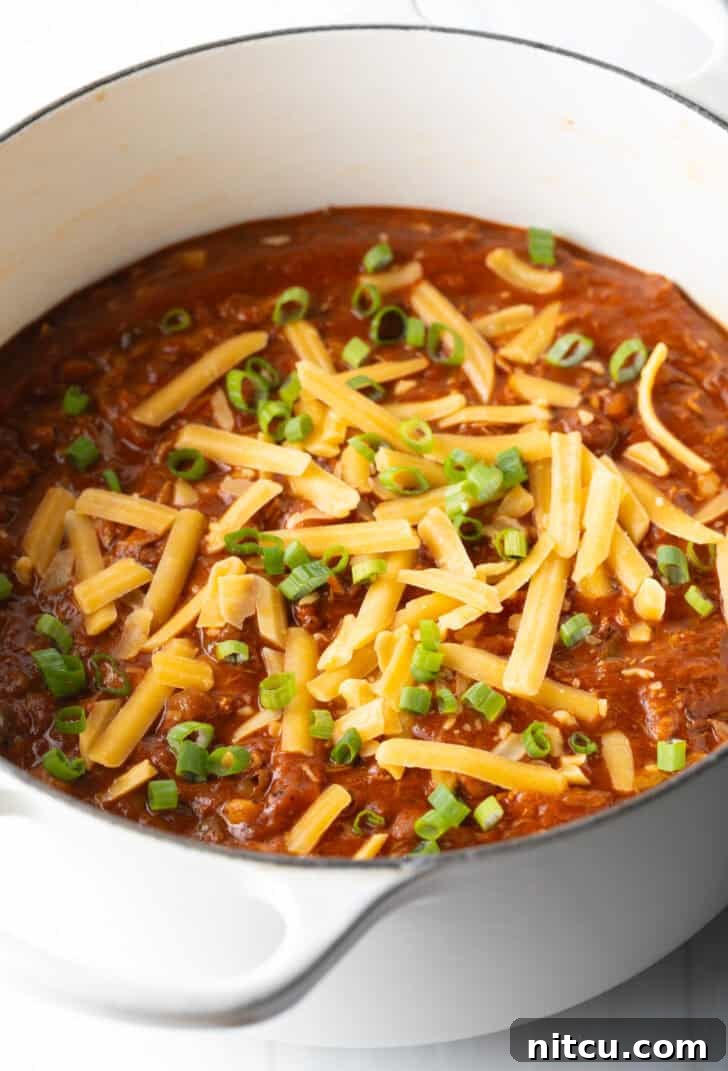 Easy 5 Ingredient Chicken Chili 11 A large, inviting white soup pot filled with the finished chicken chili, beautifully topped with fresh chopped green onions and a generous sprinkle of shredded cheddar cheese, showcasing its vibrant appeal.