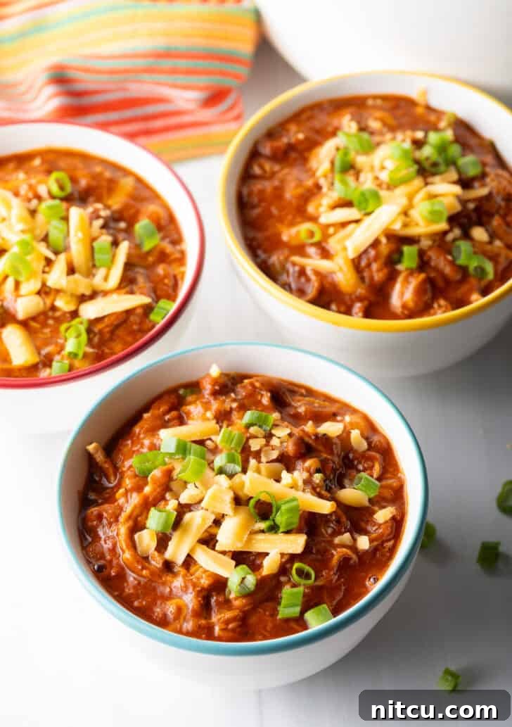 Easy 5 Ingredient Chicken Chili 4 Three perfectly portioned bowls of vibrant chicken chili, each artfully garnished with a sprinkle of chopped green onions and a generous heap of shredded cheddar cheese, ready to be enjoyed.