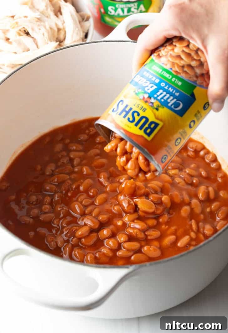 Easy 5 Ingredient Chicken Chili 6 The initial step of adding robust pinto chili beans, complete with their flavorful sauce, directly from a can into a large, sturdy pot, ready to form the base of the chili.