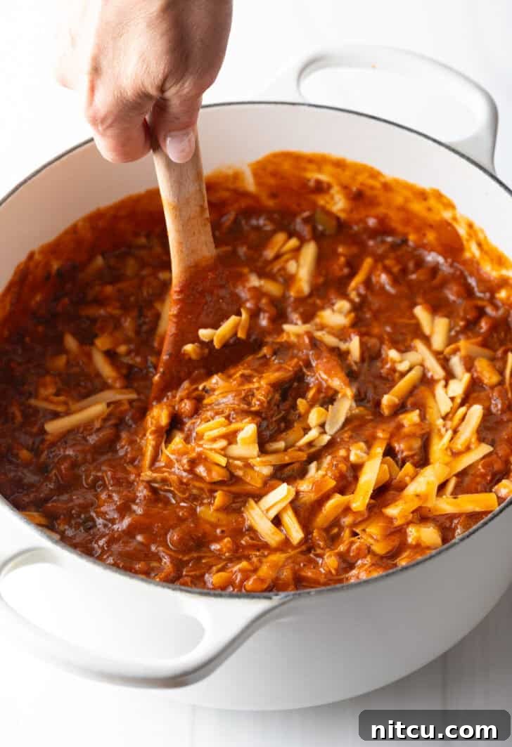 Easy 5 Ingredient Chicken Chili 10 A sturdy wooden spoon gently stirring the shredded cheese into the hot chili within the pot, demonstrating the crucial step of incorporating the cheese off the heat for a perfectly smooth and creamy finish.