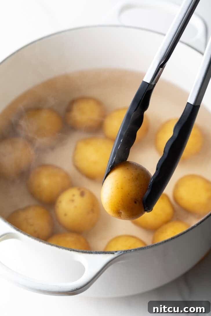 Crispy Smashed Potatoes 6 Tongs holding a small boiled potato over a large white pot with a dozen small potatoes.