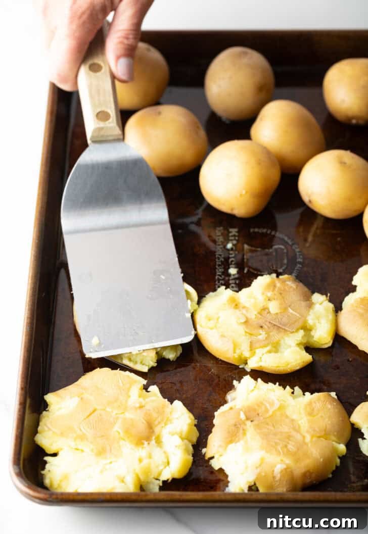 Crispy Smashed Potatoes 7 Using a metal spatula to smoosh small unbaked yellow potatoes.