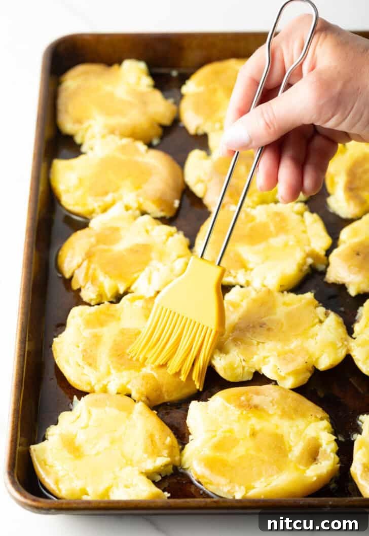 Crispy Smashed Potatoes 9 Hand using a yellow basting brush to brush ghee over smashed potatoes on a baking sheet.