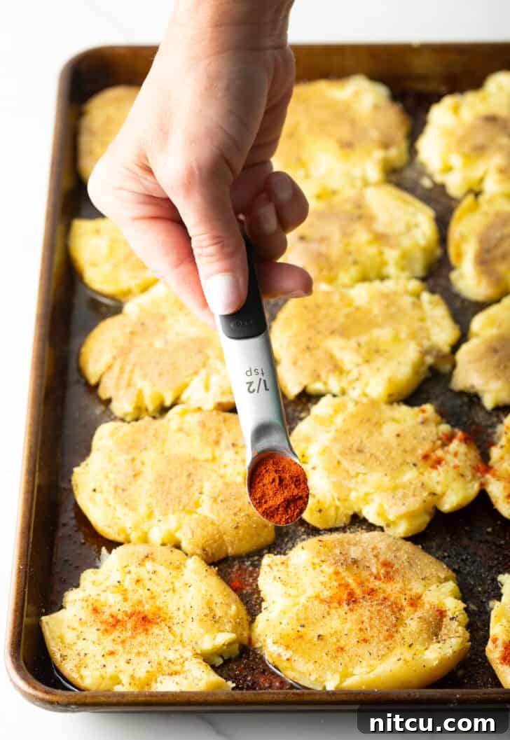 Crispy Smashed Potatoes 10 Hand adding spices from a small measuring spoon over smashed potatoes on a baking sheet.