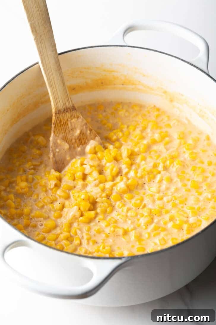 Wooden spatula stirring creamed corn in a large white pot, close up.