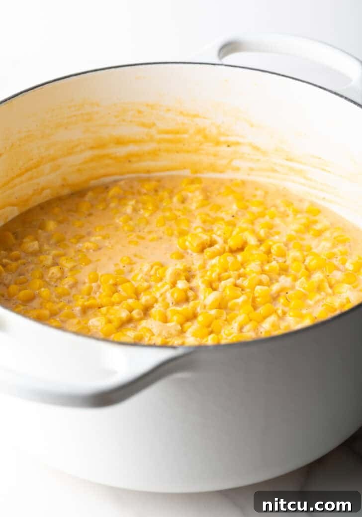 Creamed corn simmering in a large white pot, showing the thick, creamy sauce.