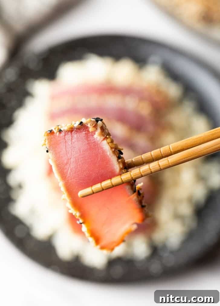 Flash-Seared Ahi Tuna 2 Close-up of a succulent slice of sesame-crusted seared yellowfin tuna held by chopsticks.