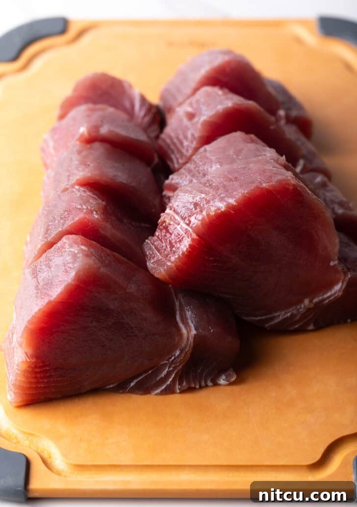 Flash-Seared Ahi Tuna 7 Slices of raw ahi tuna uniformly cut on a cutting board.