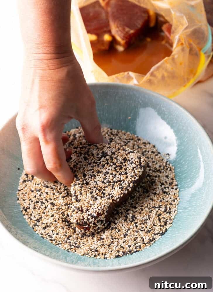 Flash-Seared Ahi Tuna 10 A hand gently pressing a raw piece of ahi tuna steak into a bowl filled with tricolor sesame seeds for an even coating.