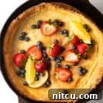 Top-down view of a Dutch Baby in a cast iron skillet, topped with strawberries, blueberries, and lemon slices.