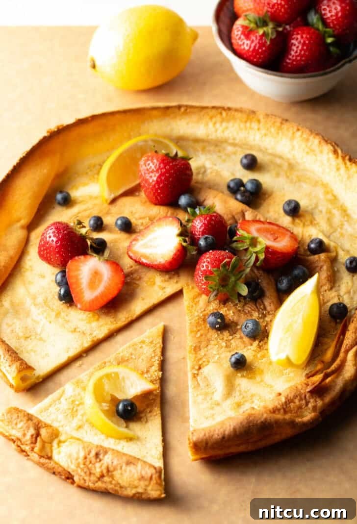 Effortless Puffed Pancake Perfection 4 A baked Dutch Baby pancake on a wooden cutting board, adorned with fresh strawberries and blueberries. One wedge has been pulled aside, showing its tender layers.