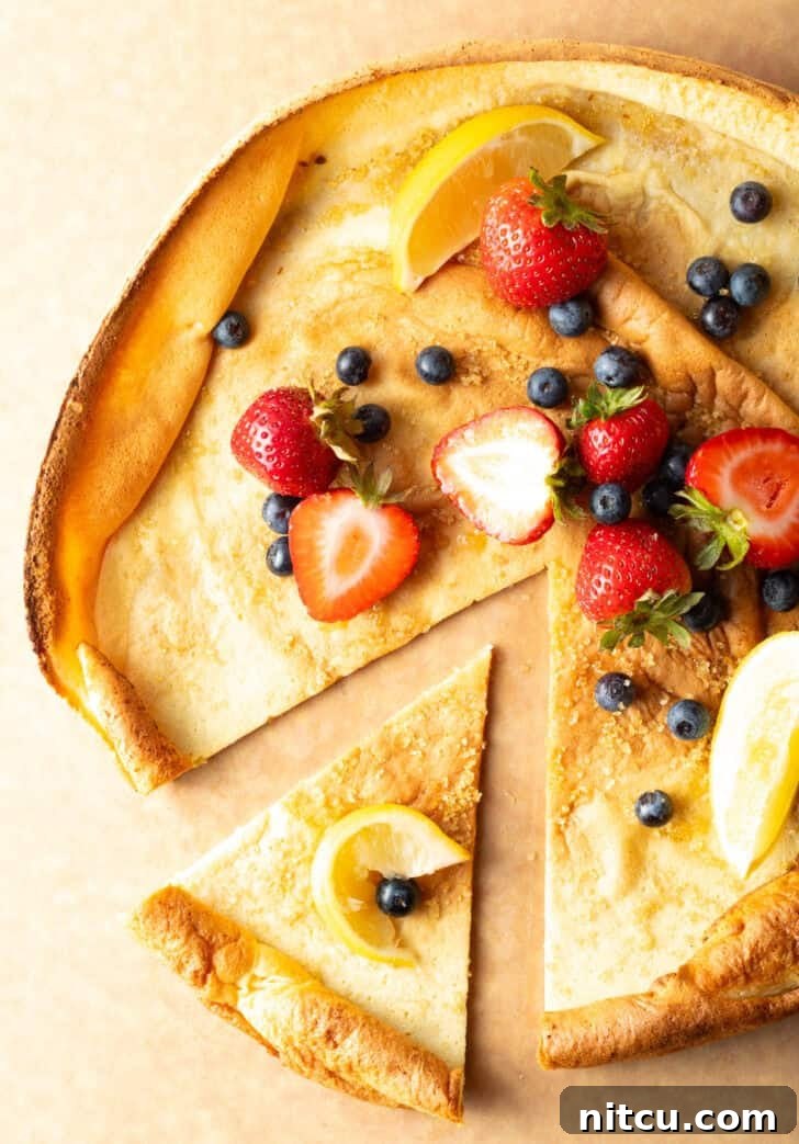 Effortless Puffed Pancake Perfection 9 Top-down view of a Dutch Baby on a cutting board, garnished with fresh strawberries and blueberries. A slice has been removed, revealing its inviting texture.