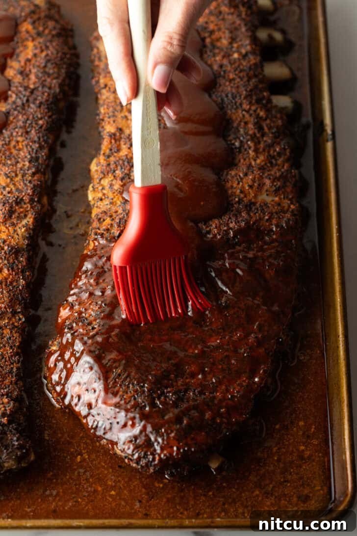 Gateway City Ribs 11 St. Louis-style ribs on an oven tray being brushed with barbecue sauce for the final glaze.